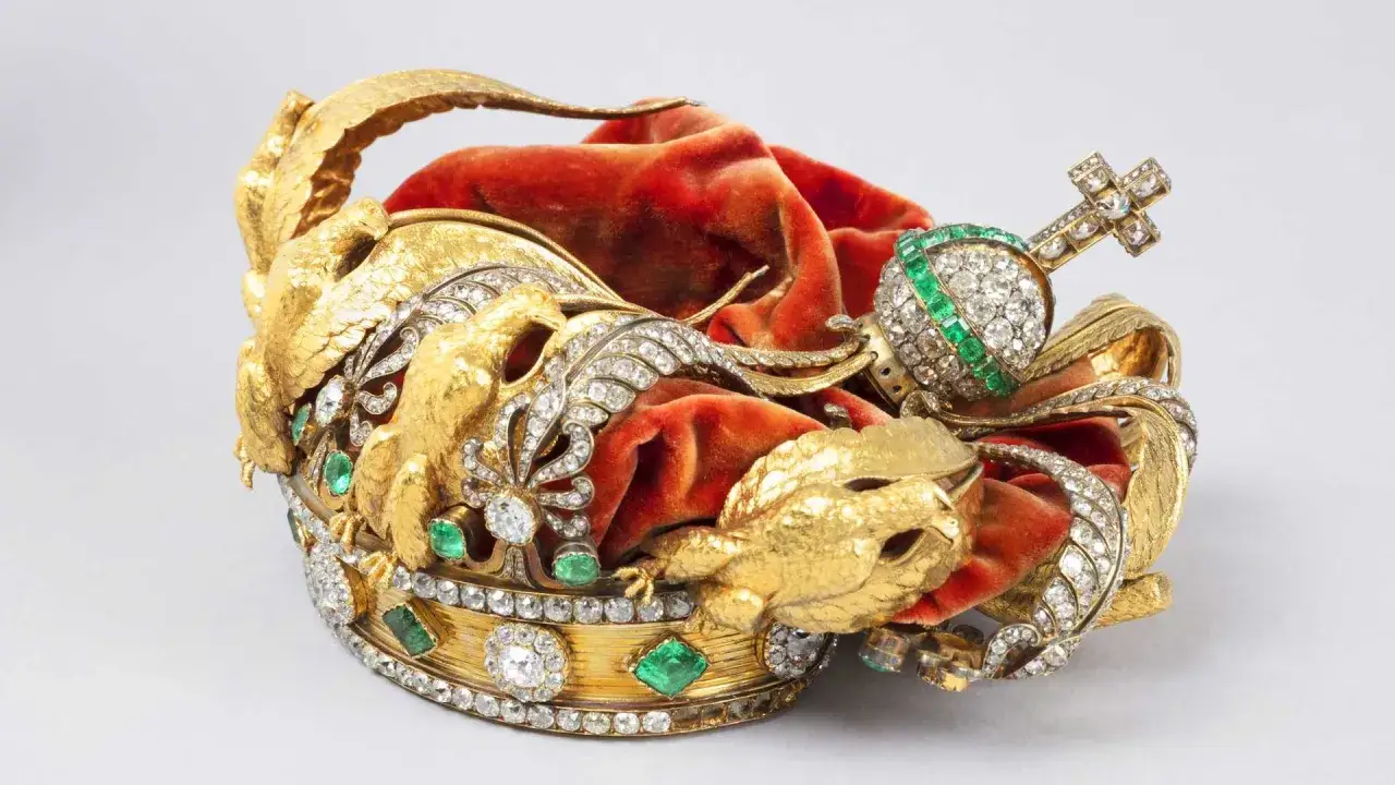 Magnifique couronne de l'impératrice Eugénie, ornée d'aigles dorés, de diamants et d'émeraudes, posée sur un velours rouge.