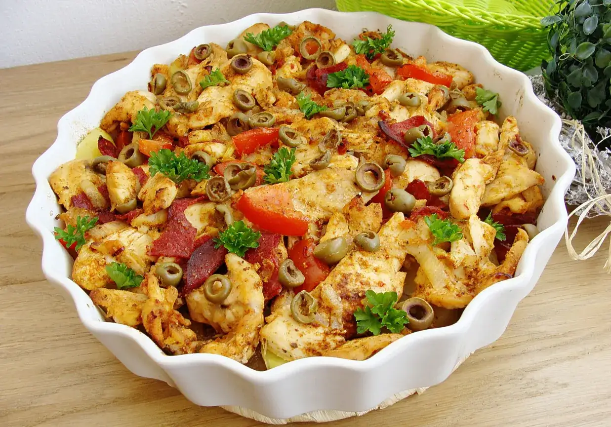 Pyszna zapiekanka z chorizo, kurczakiem, pomidorami i oliwkami, udekorowana natką pietruszki.