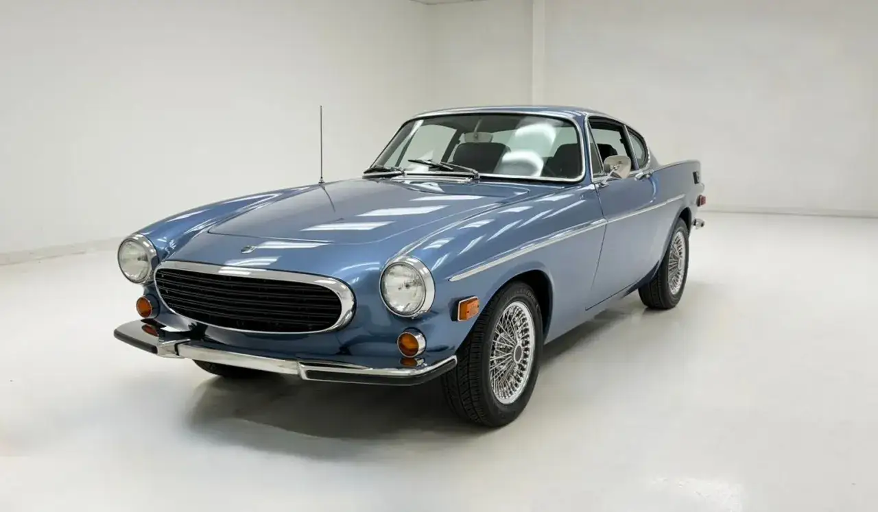 Błękitne Volvo P1800 z chromowanymi felgami i grillem, klasyk z lat 70. na białym tle.