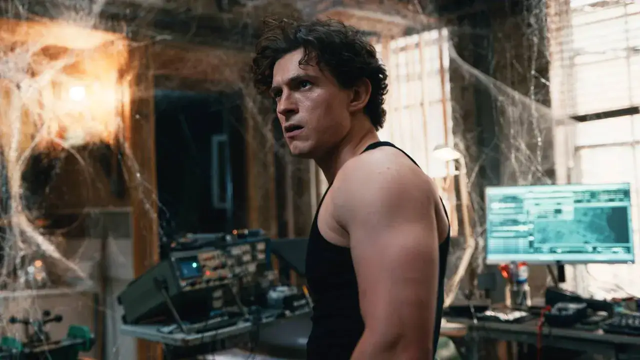 Tom Holland i en mörk tanktopp, omgiven av spindelväv och teknisk utrustning. En scen från filmer med Tom Holland.