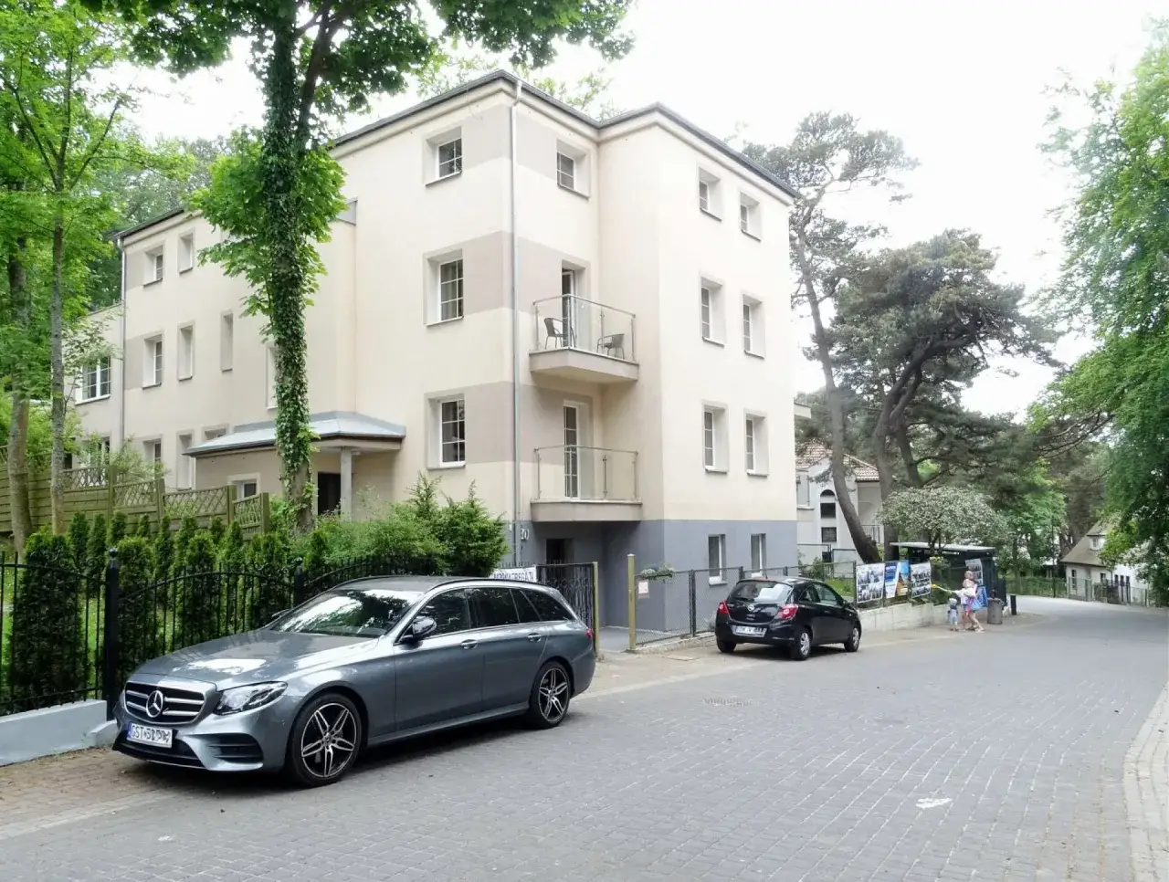 Nowa Fregata Pokoje i Apartamenty: nowoczesny budynek z balkonami, otoczony zielenią. Przed posesją stoją dwa samochody.