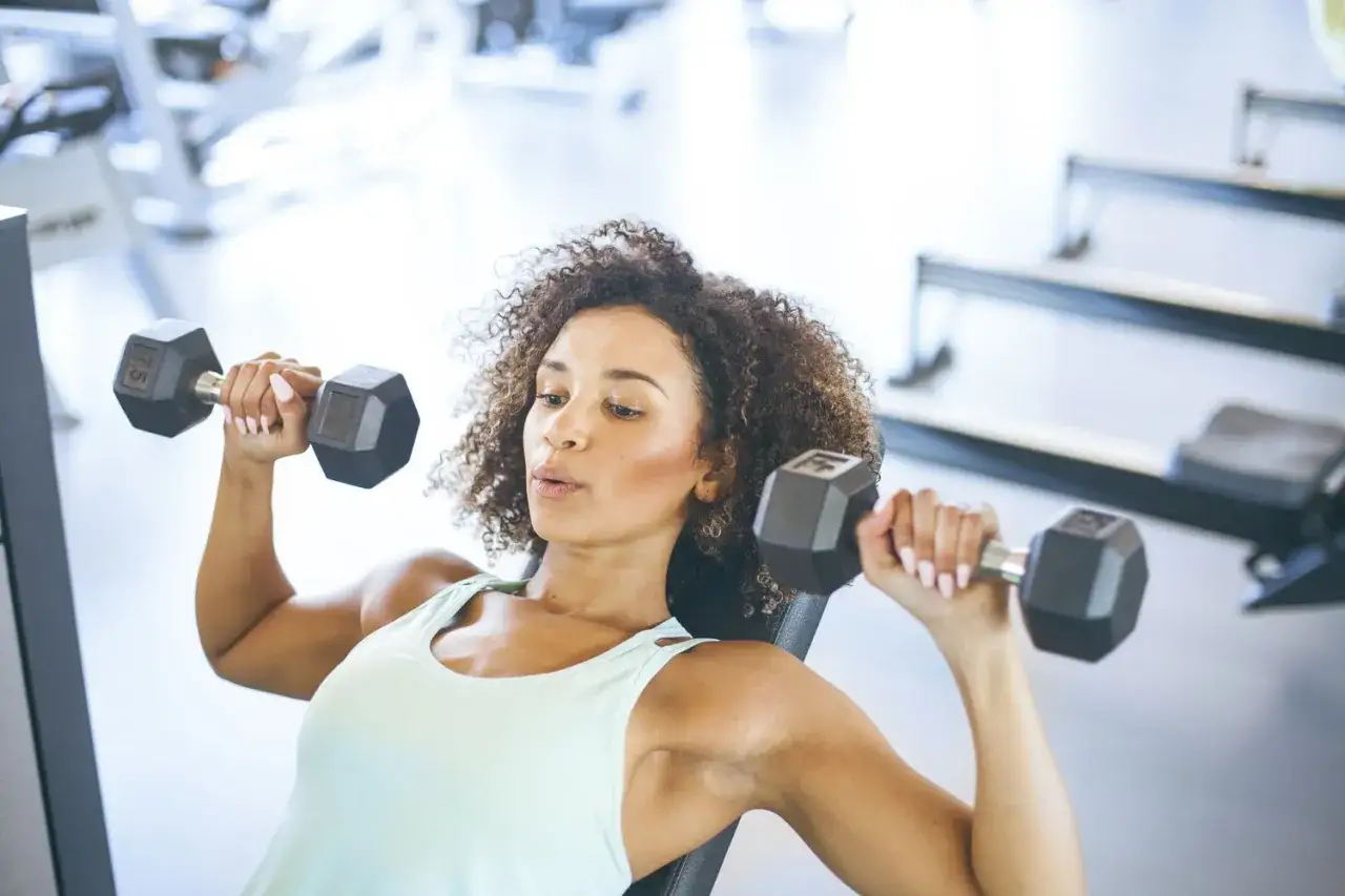 Donna con fisico magro e definito si allena in palestra con i manubri.
