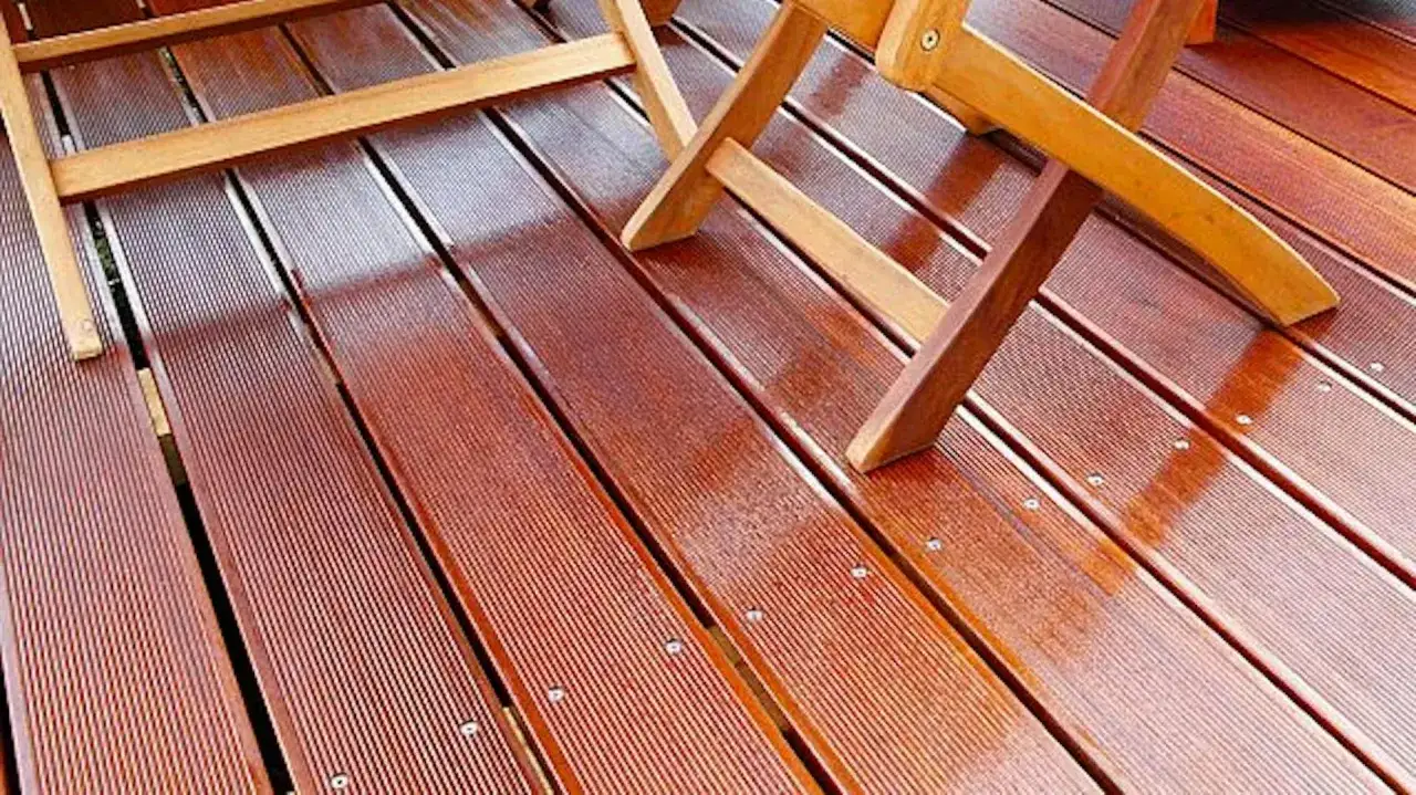 Drewniany taras lśni dzięki dobremu lakierowi do drewna na zewnątrz. Widać fragmenty drewnianych mebli.