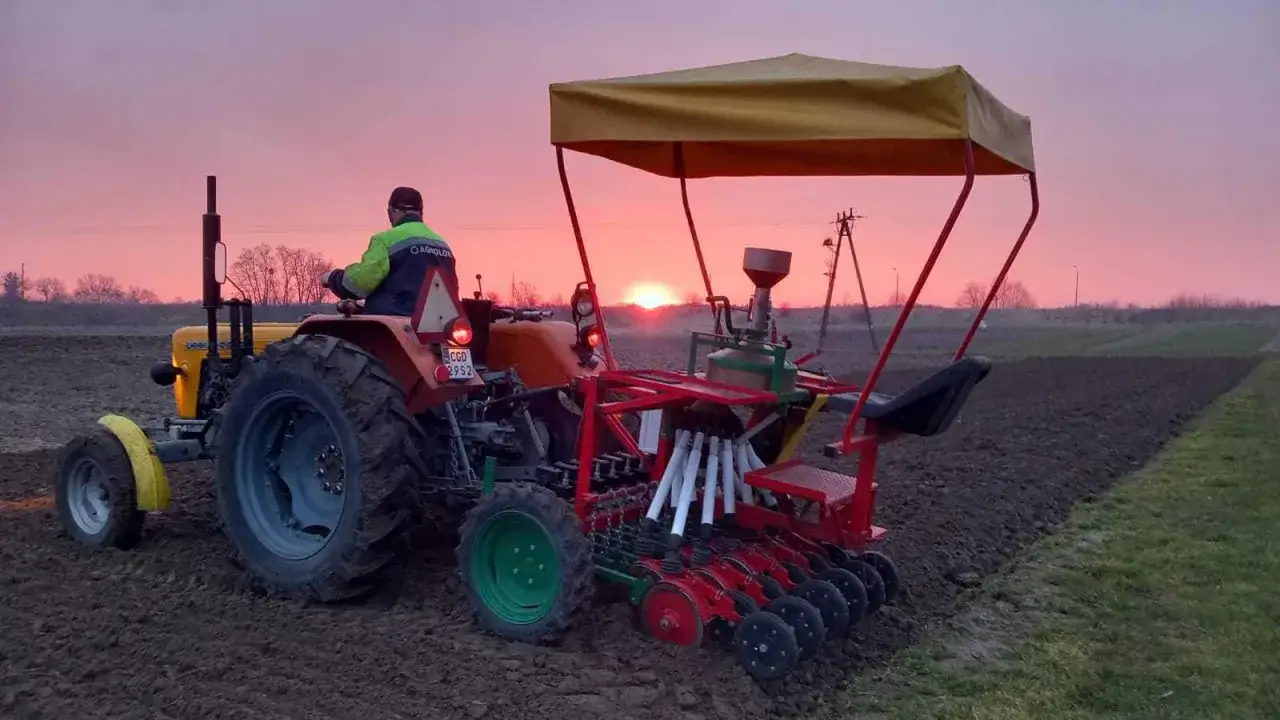 Traktor z siewnikiem wschodzącego słońca. Rolnik wyznacza ścieżki technologiczne, przygotowując pole do siewu.