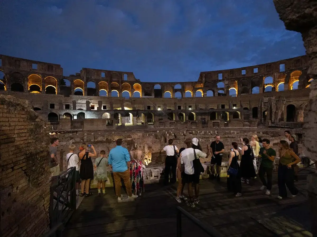 Visite du Colisée de Rome en août, illuminé à la tombée de la nuit. Des touristes admirent l'architecture antique.