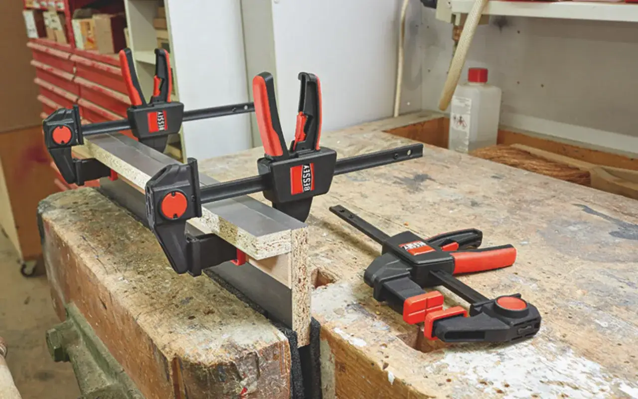 Trois serre-joints Bessey, outils pour travailler le bois, maintiennent fermement des planches sur un établi.