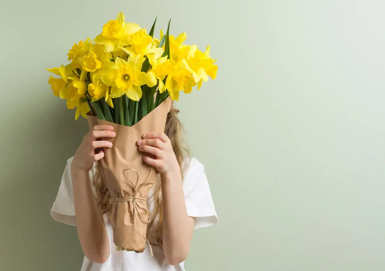 Un enfant cache son visage derri&egrave;re un bouquet de jonquilles jaunes, symboles de renouveau et d'espoir.