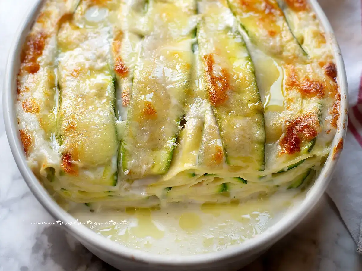 Lasagne di verdure appena sfornate, con zucchine e formaggio filante, in una teglia bianca.