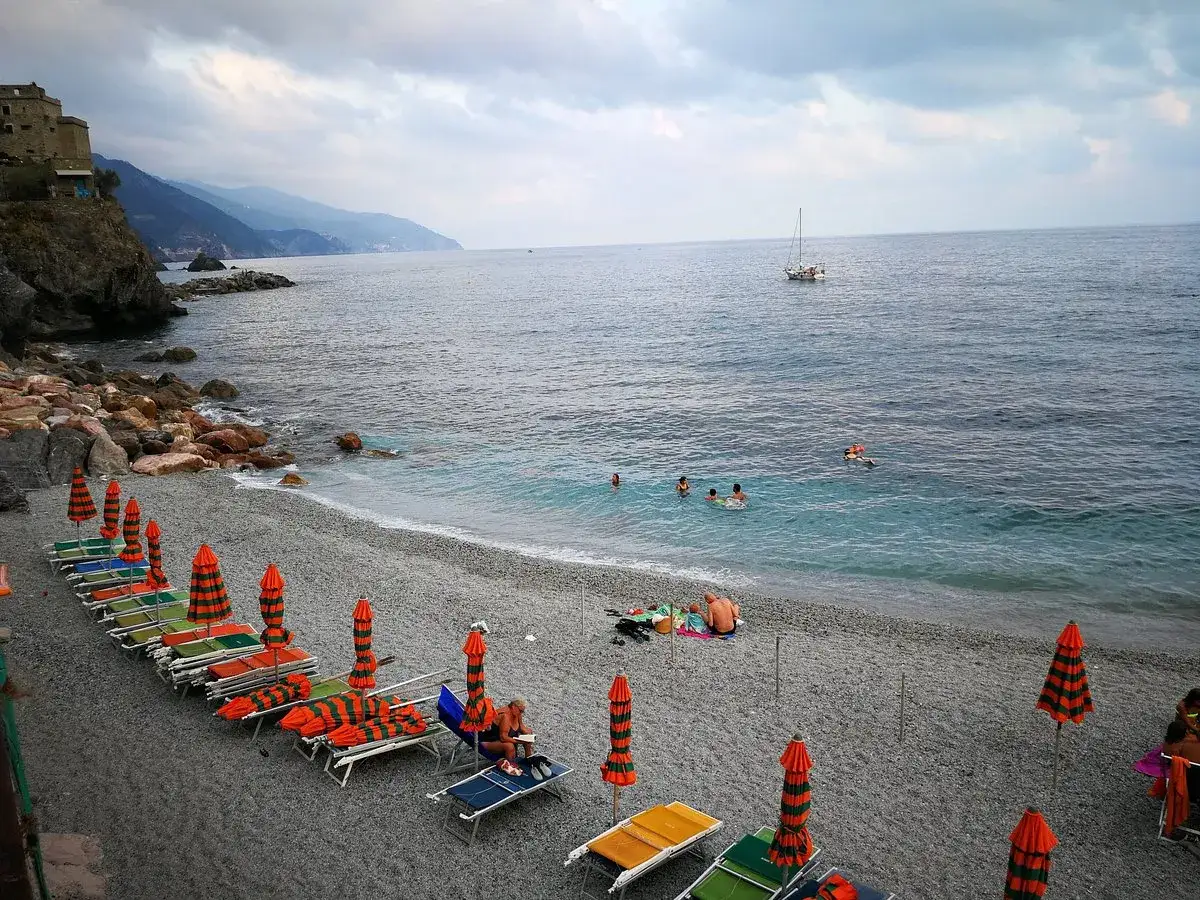 Ombrelloni e lettini sulla monterosso spiaggia libera, con persone che nuotano e una barca a vela in lontananza.