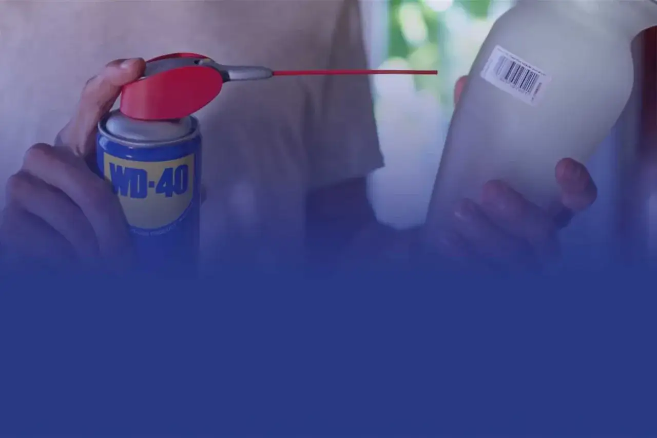 WD-40 Dose mit rotem Spr&uuml;haufsatz wird auf ein Glas mit Etikett gehalten. So l&auml;sst sich ein Aufkleber von Glas entfernen.