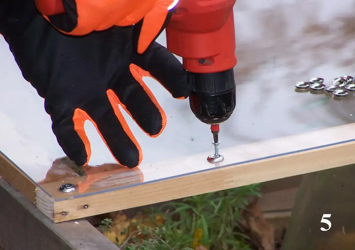 Using a drill and screws to attach plexiglass to wood. A gloved hand guides the drill.