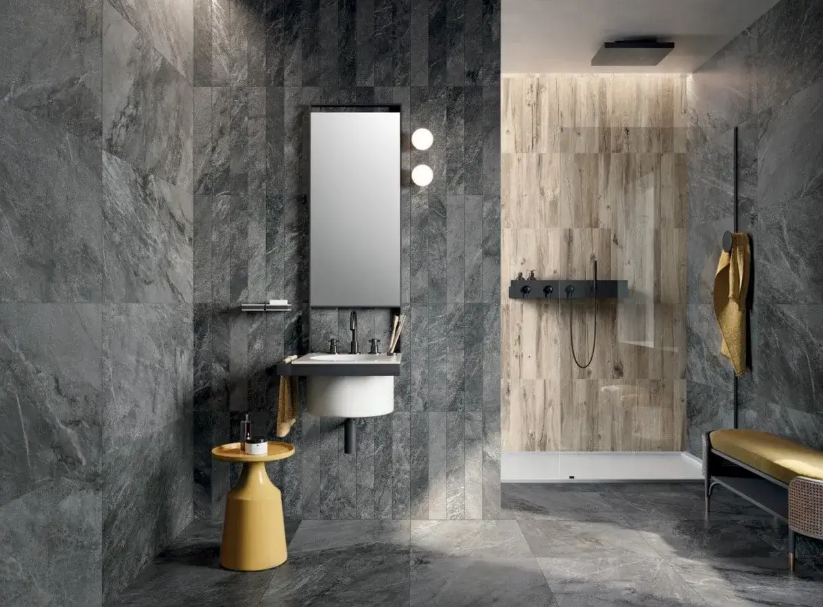 Modernes Bad mit grauen Marmorfliesen und Holzakzenten. Ein gelber Beistelltisch sorgt f&uuml;r einen Farbtupfer. Eine Dusche mit Holzwand und schwarzer Armatur. Bad-Inspo, die polarisiert.