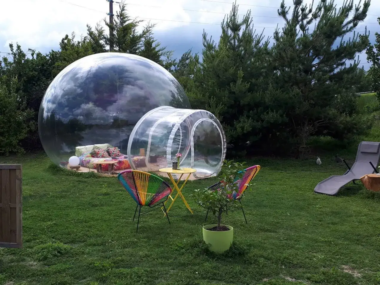 Une bulle transparente invite à une nuit étoilée en Île-de-France. Un espace cosy avec coussins et table basse, prêt pour l'aventure.