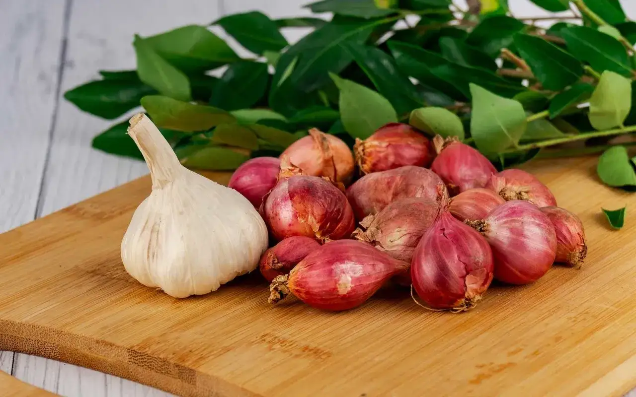 Knoblauch und Schalotten auf einem Holzbrett, bereit als ohrenschmerzen hausmittel. Grüne Blätter im Hintergrund.