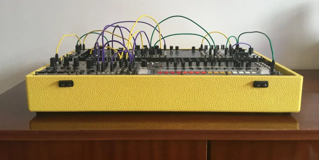 Gelbes Geh&auml;use mit vielen Kn&ouml;pfen, Schaltern und Kabeln, die f&uuml;r **modular synthesis** verbunden sind.
