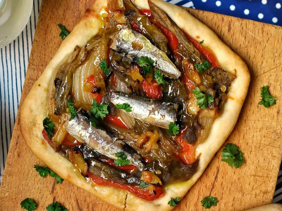 Coca de recapte con verduras asadas y sardinas, decorada con perejil fresco.