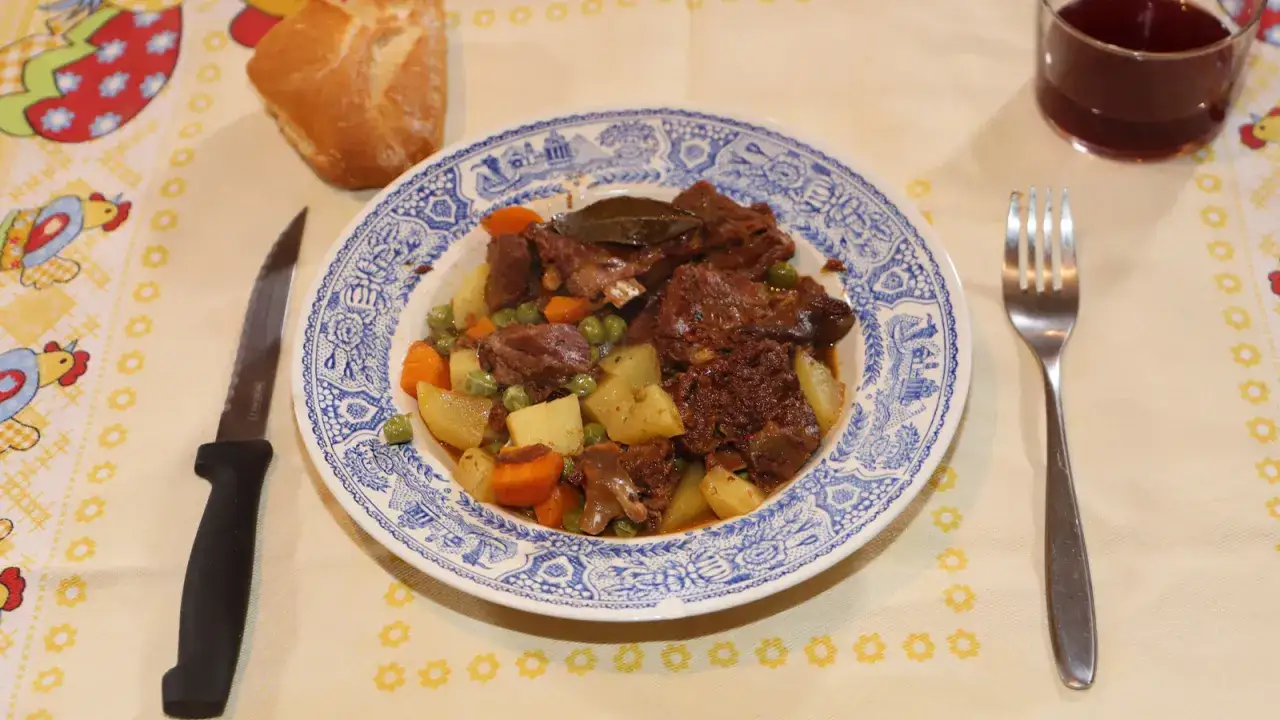 Un plato con las mejores recetas de corzo guisado, acompa&ntilde;ado de patatas, zanahorias y guisantes. Servido con pan y vino tinto.