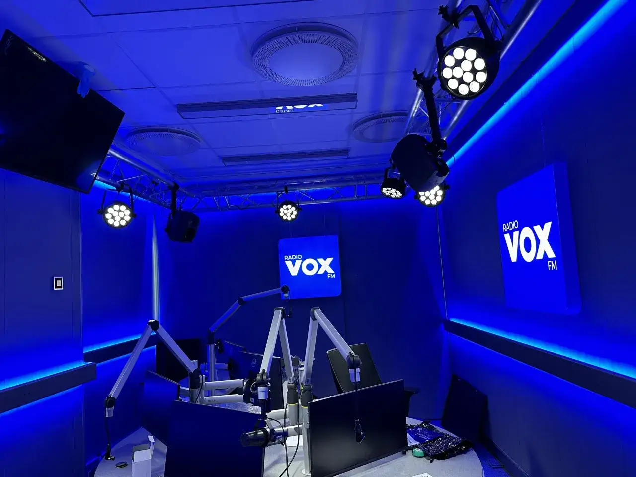 Studio radiowe VOX FM Warszawa w niebieskim świetle. Widać mikrofony, monitory i logo stacji.
