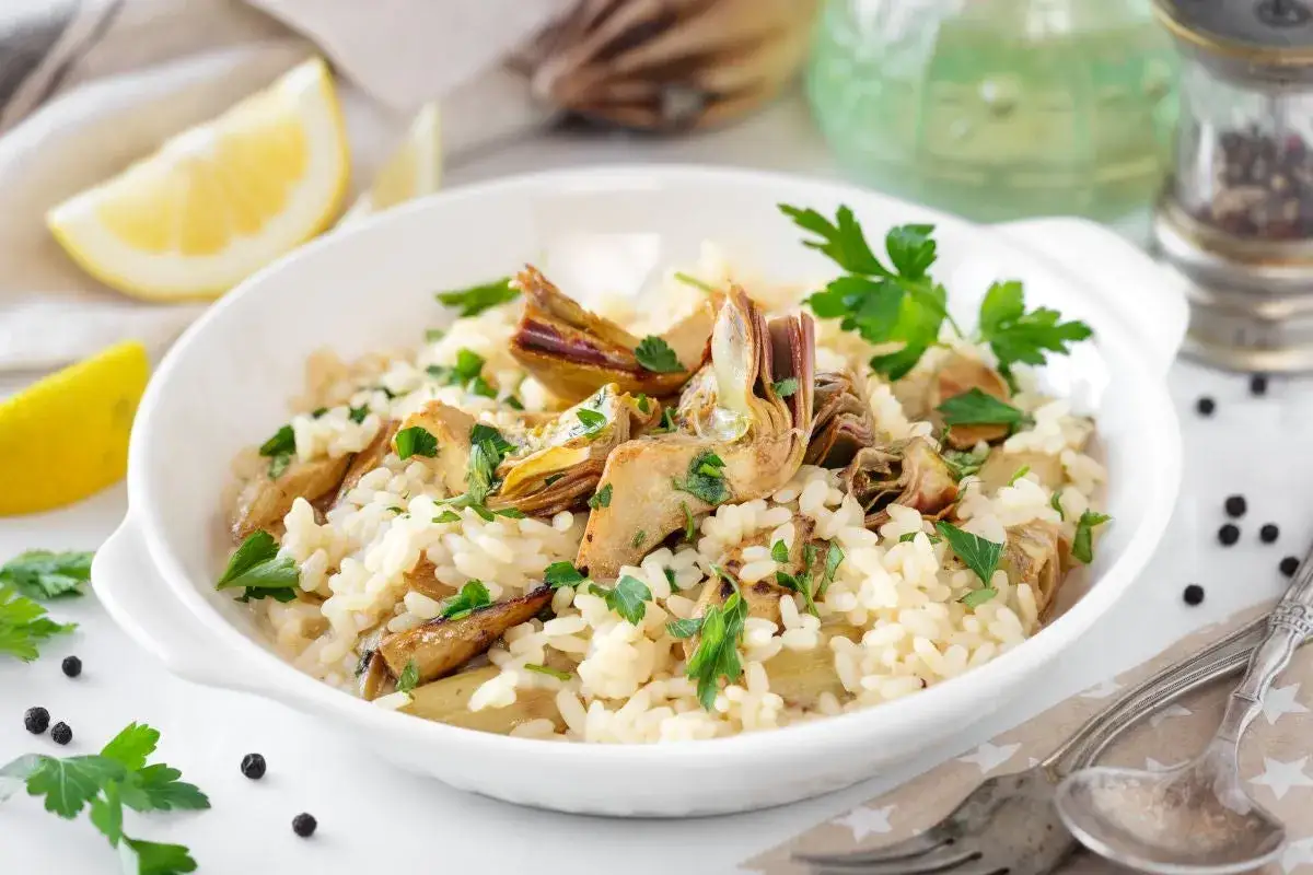 Un cremoso risotto con carciofi freschi, guarnito con prezzemolo e spicchi di limone.