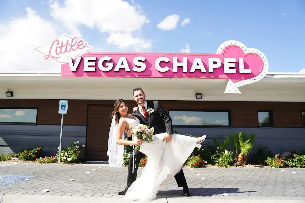 Szczęśliwa para po ślubie w Las Vegas, pan młody trzyma pannę młodą na rękach przed kaplicą.