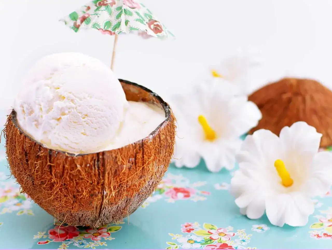 Delicioso helado de coco servido en su cáscara, adornado con una sombrilla tropical y flores blancas.