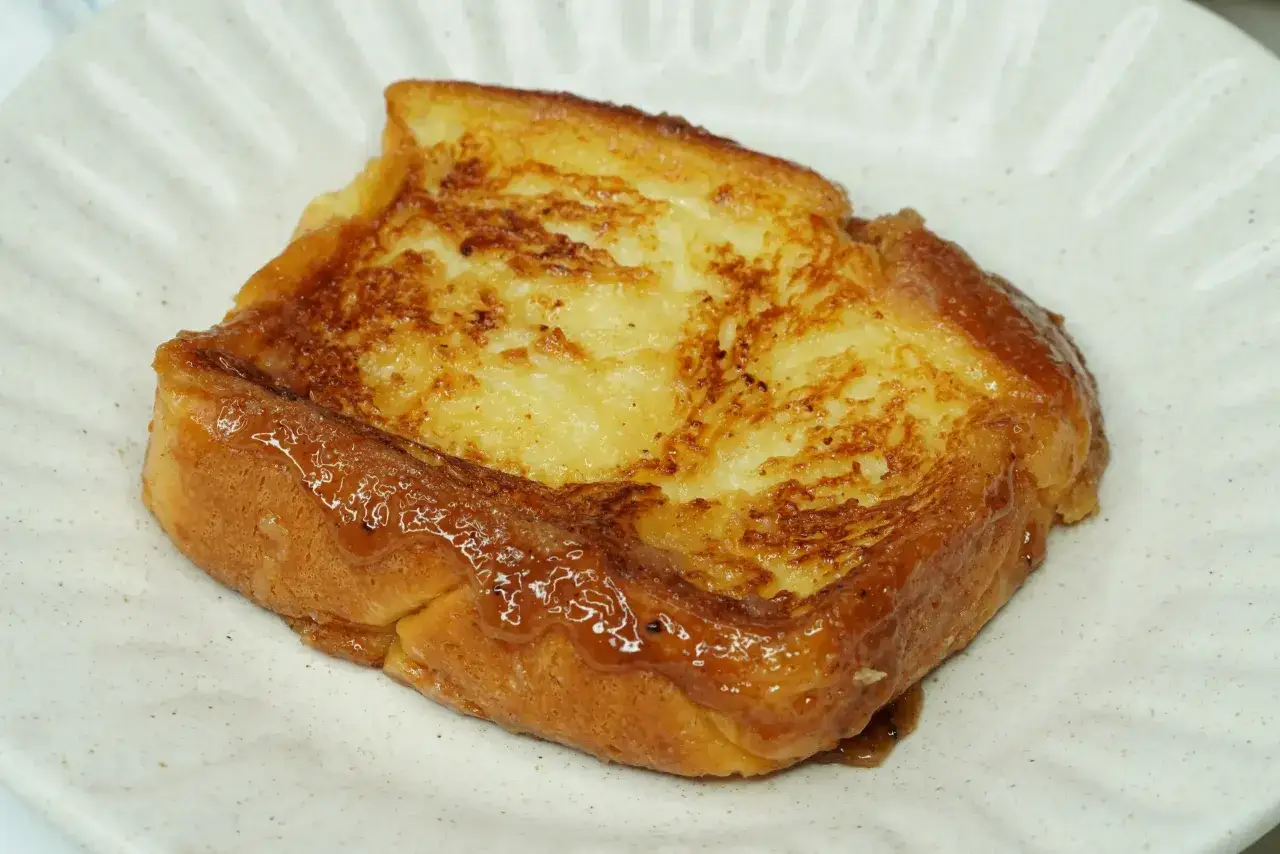 Un delicioso pan de calatrava dorado y caramelizado, servido en un plato blanco con un borde texturizado.