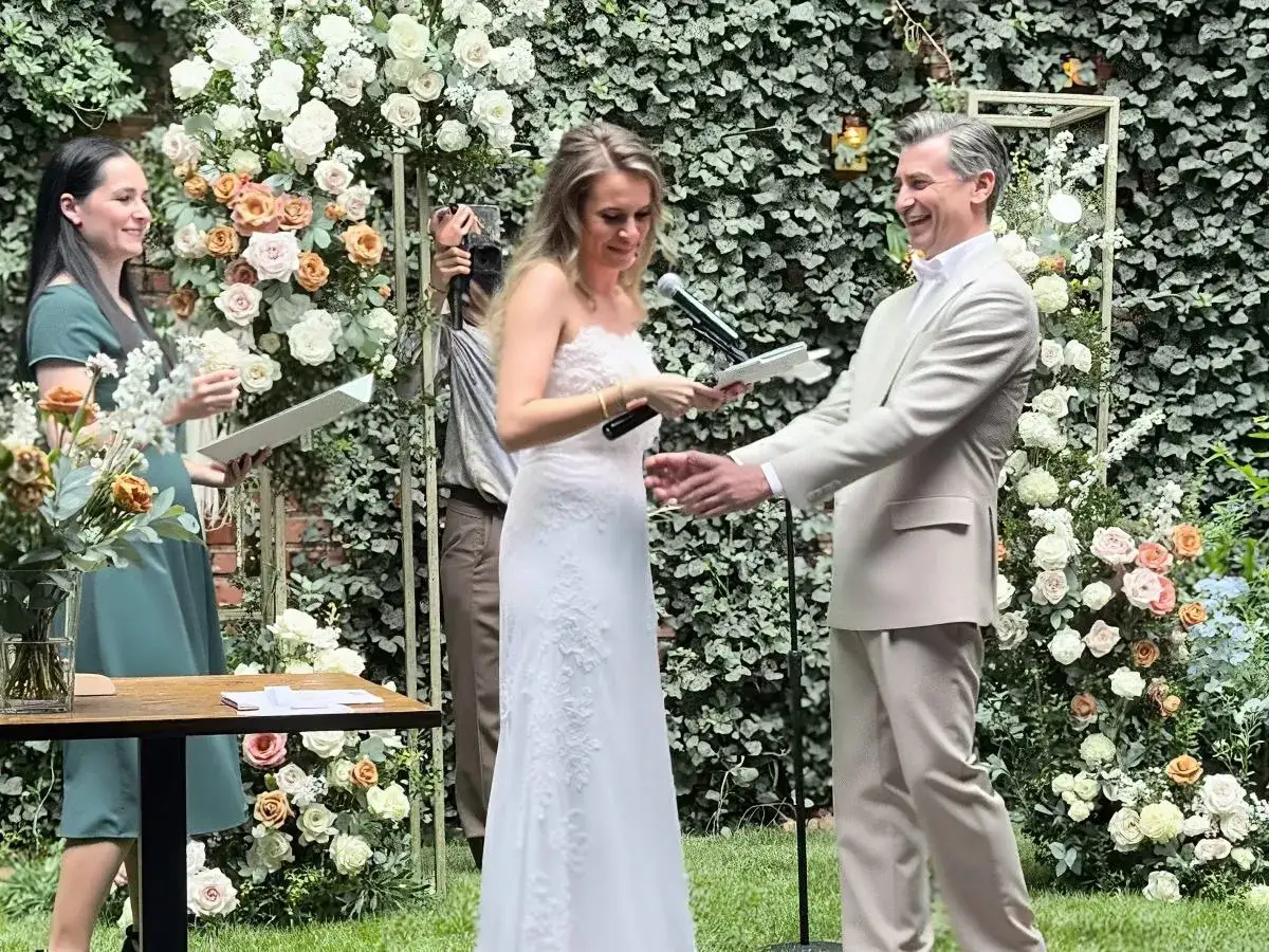 Piotr Bajtlik i jego żona podczas ceremonii ślubnej, otoczeni bujną zielenią i kwiatami.