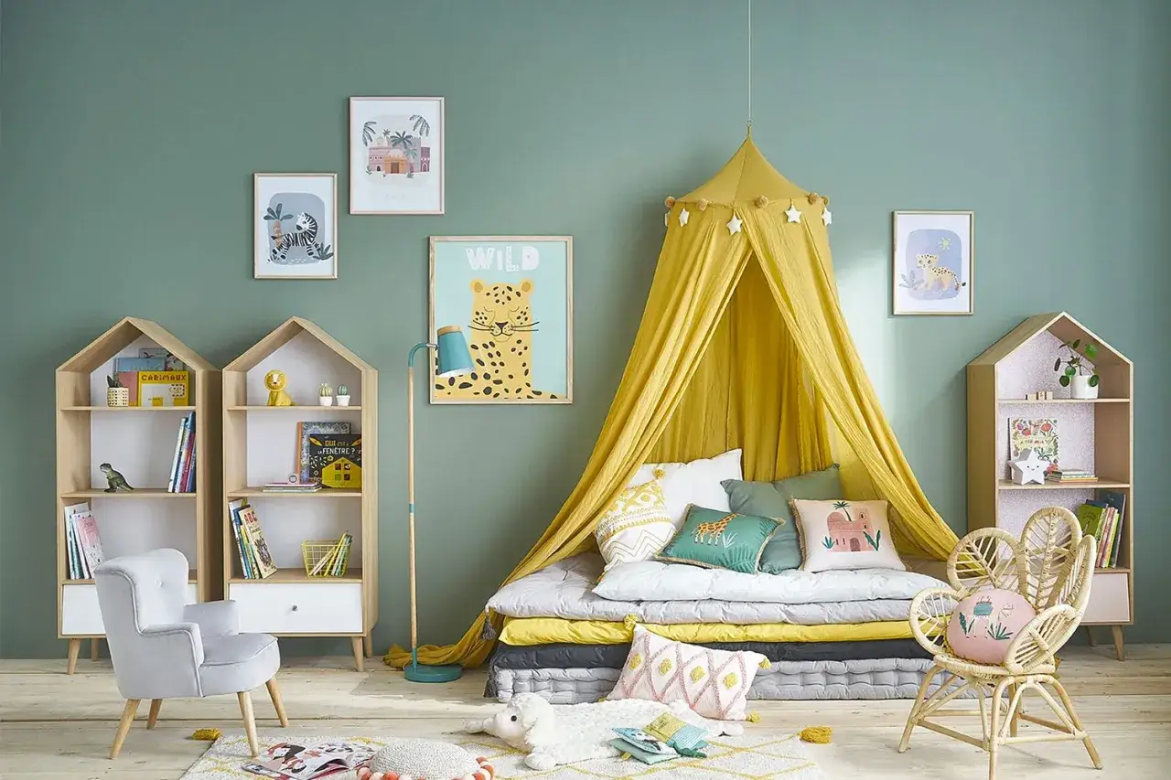 Aménagement chambre enfant : un lit au sol sous un ciel de lit jaune, des étagères en forme de maison, et des décorations sauvages pour une ambiance joyeuse.