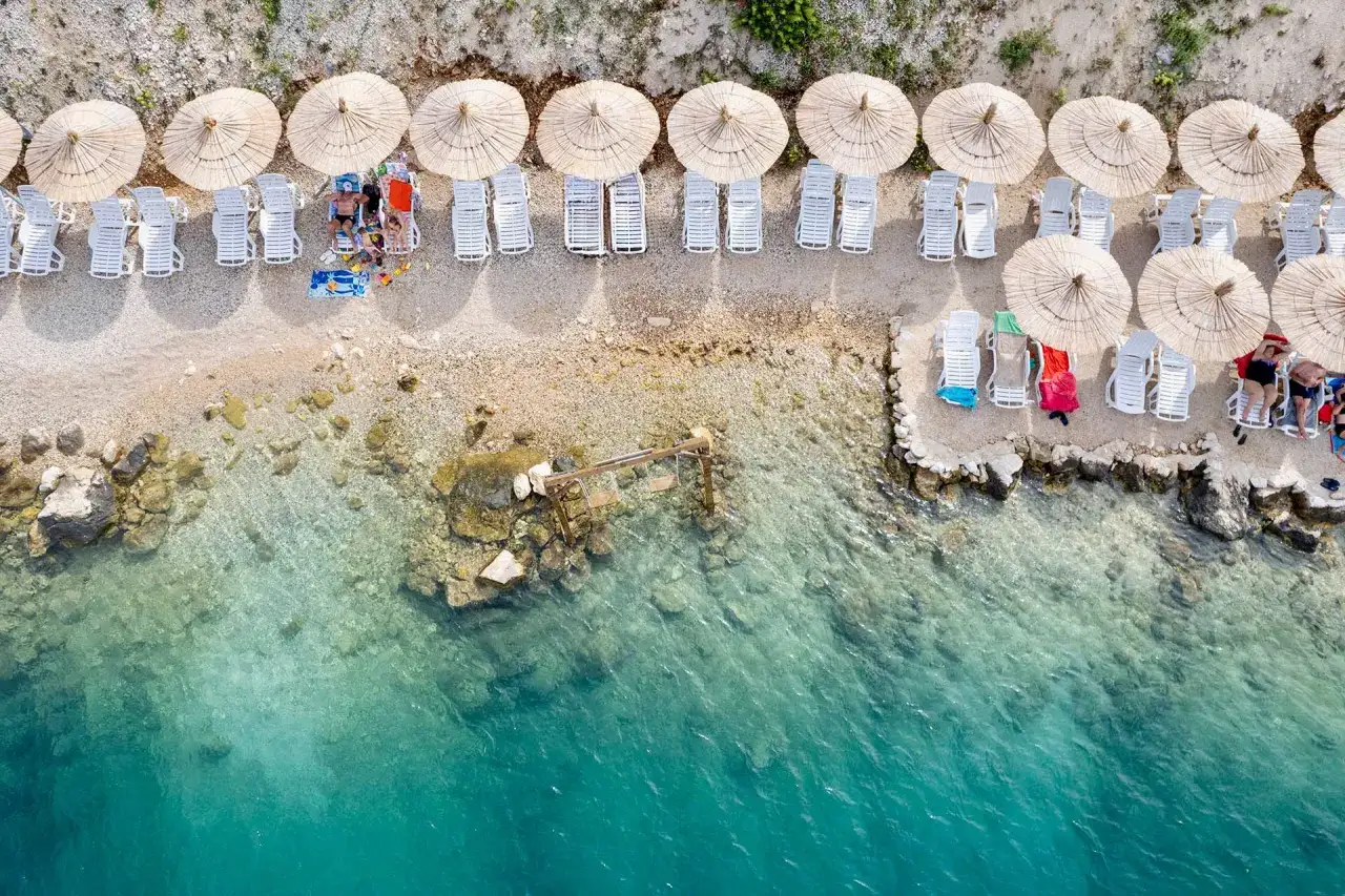 Słoneczny dzień na plaży w Neum, Bośnia i Hercegowina. Leżaki pod parasolami, turkusowa woda.