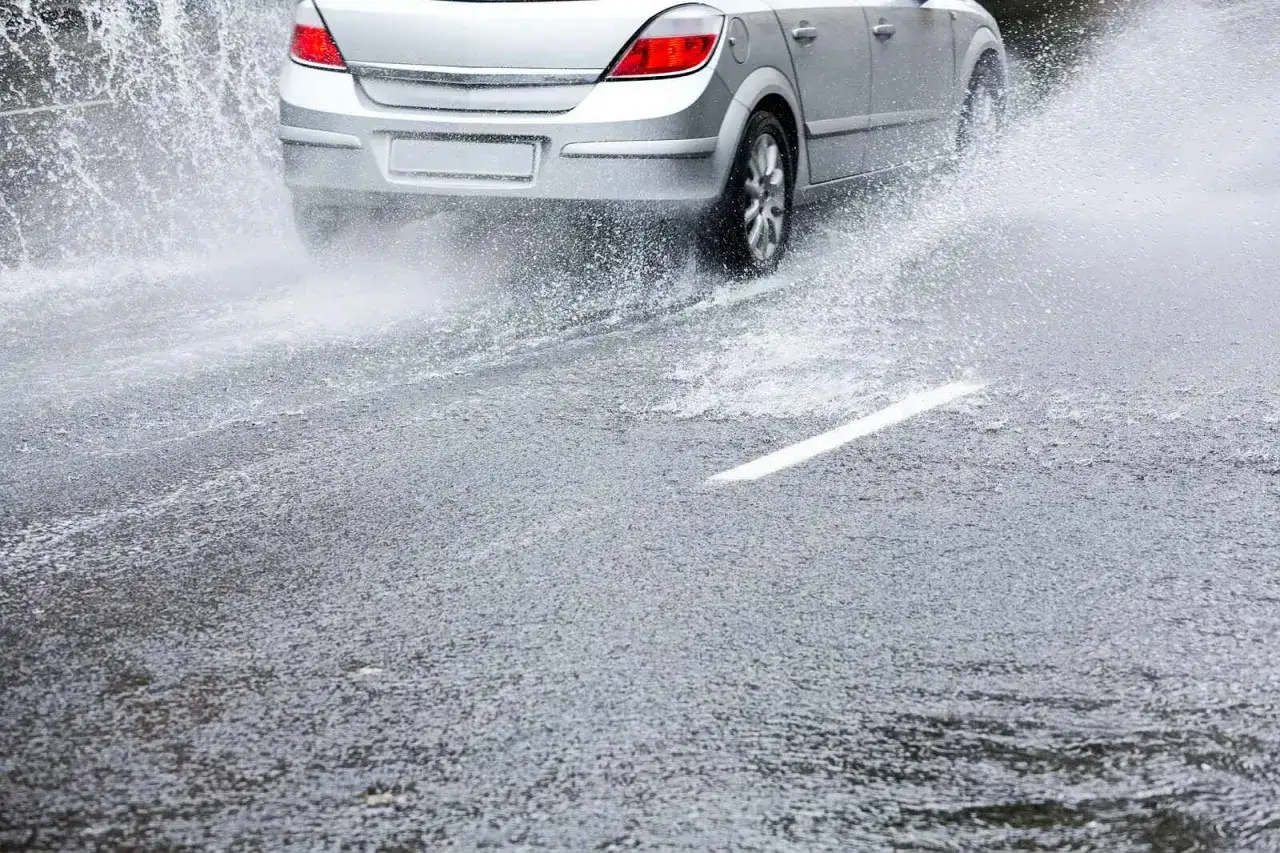 Coche plateado en carretera mojada, levantando una gran cortina de agua. Peligro de aquaplaning que es.