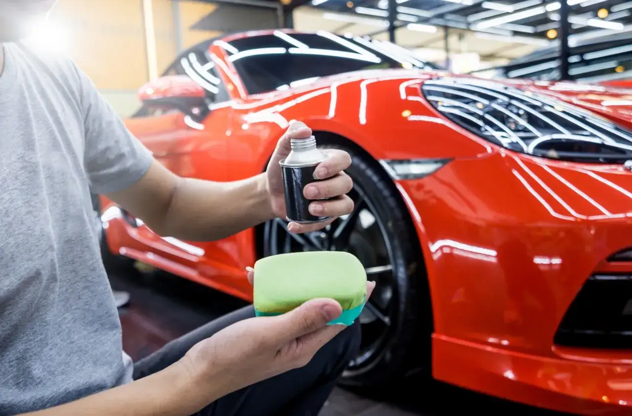 Mężczyzna przygotowuje się do detailingu czerwonego Porsche, aplikując na gąbkę środek z alkoholem izopropylowym.