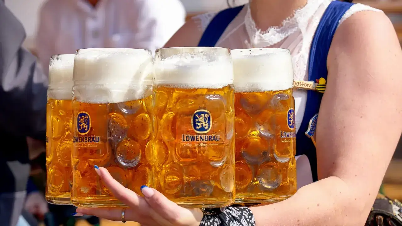 Vier Ma&szlig;kr&uuml;ge mit L&ouml;wenbr&auml;u-Bier, das typischerweise um die 6% Alkohol hat, werden von einer Kellnerin im Dirndl getragen.