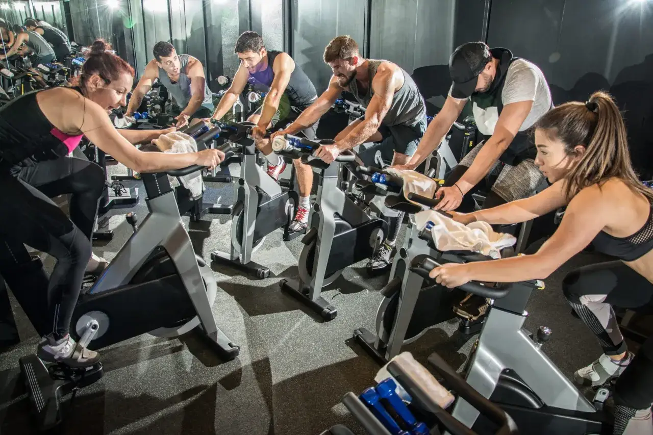 A group of people engage in an intense indoor cycling class, a popular form of spinning, pushing their limits in a gym setting.