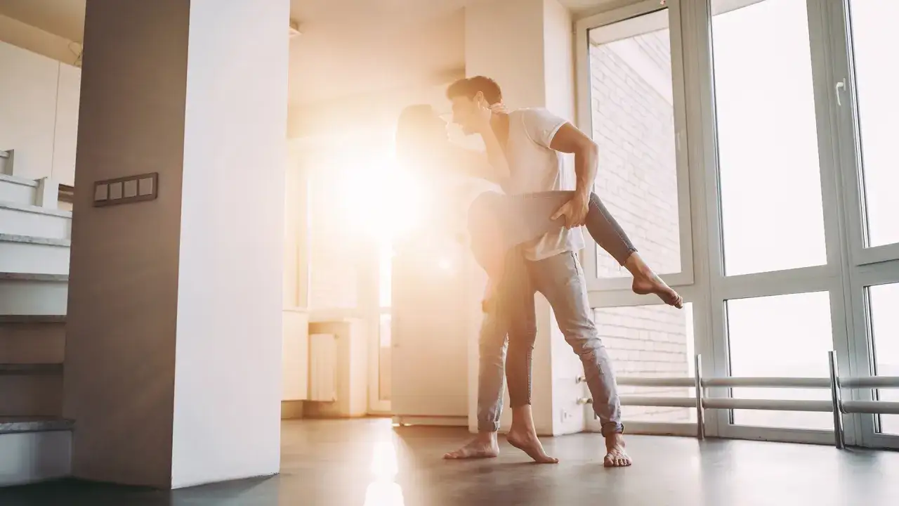 Una pareja baila apasionadamente en su hogar, reflejando la alegr&iacute;a de la convivencia.