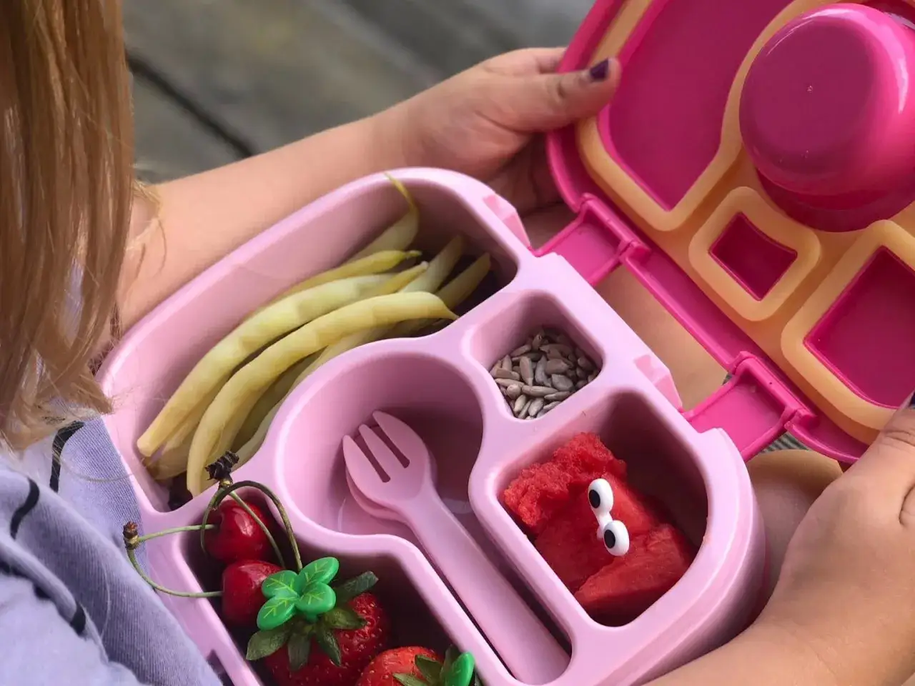 Różowy lunchbox z fasolką, wiśniami, truskawkami, pestkami i arbuzem z oczkami. Świetny pomysł na śniadanie dla dziecka!