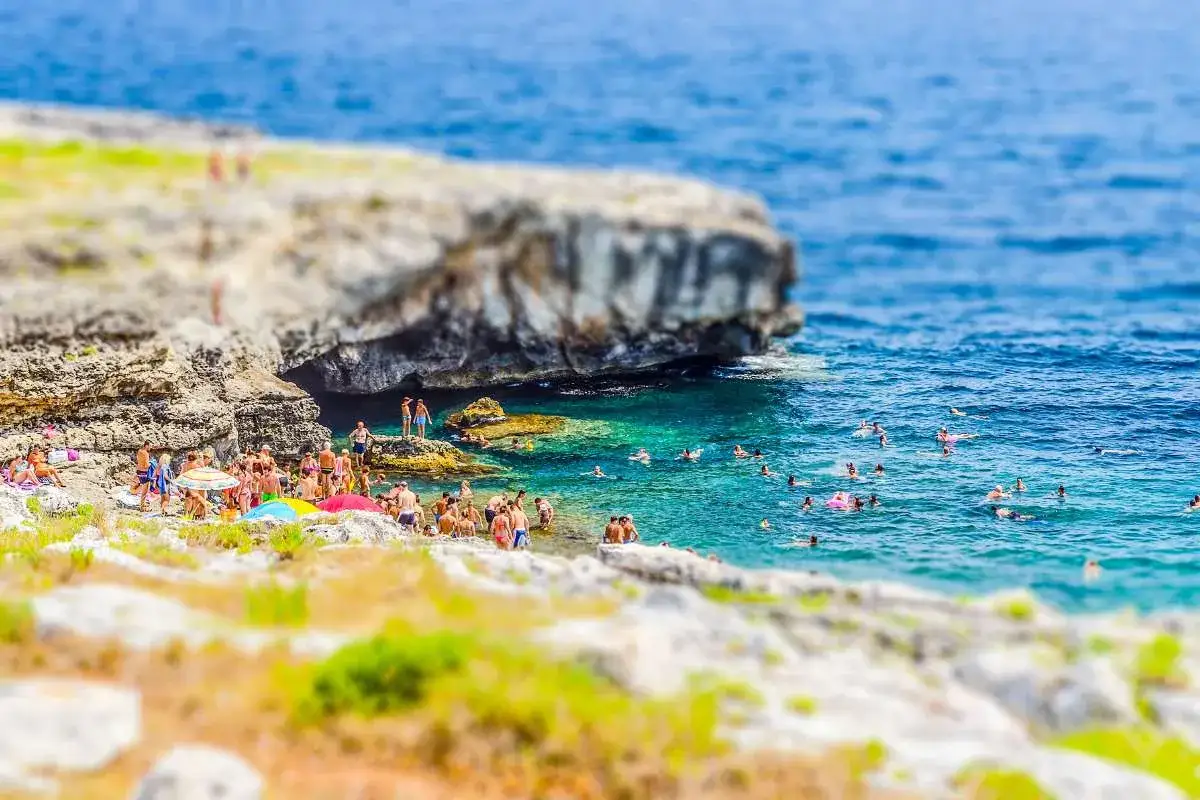 Gente che si gode il sole e il mare cristallino nella spiaggia della Grotta Verde, tra scogli e acque turchesi.