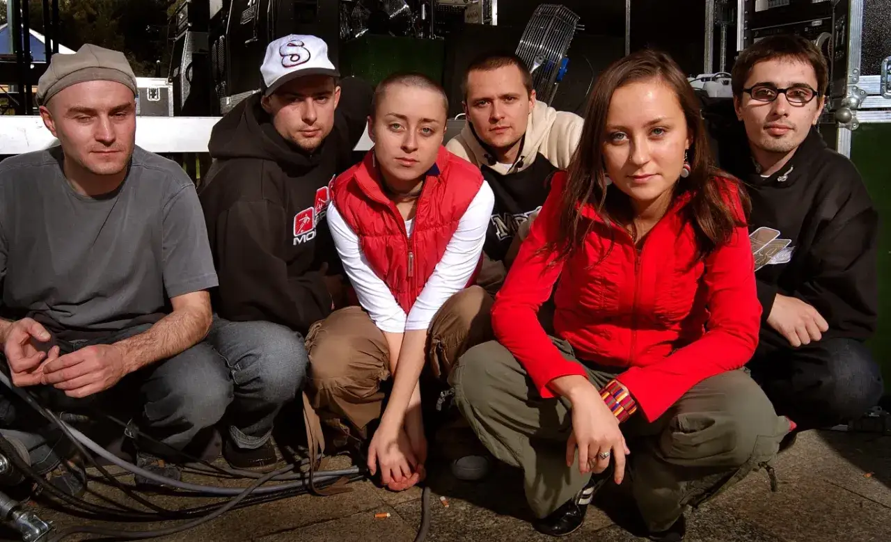 Grupa przyjaciół, w tym siostry przybysz, siedzi na ziemi przed sceną.