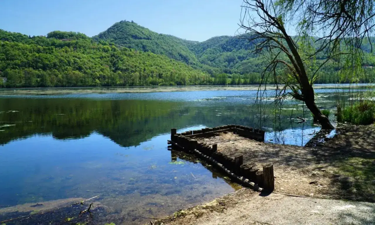 Un pontile in legno sul lago di Fimon, circondato da colline verdi e alberi rigogliosi sotto un cielo azzurro.