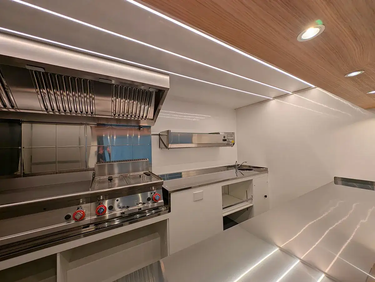 Interno di un food truck pronto per aprire: cucina professionale in acciaio inox, cappa aspirante e piano di lavoro.