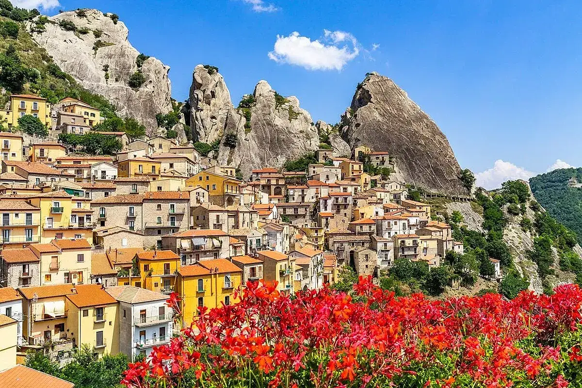 Castelmezzano cosa vedere: un borgo incantevole aggrappato alle rocce, con case colorate e fiori rossi in primo piano.