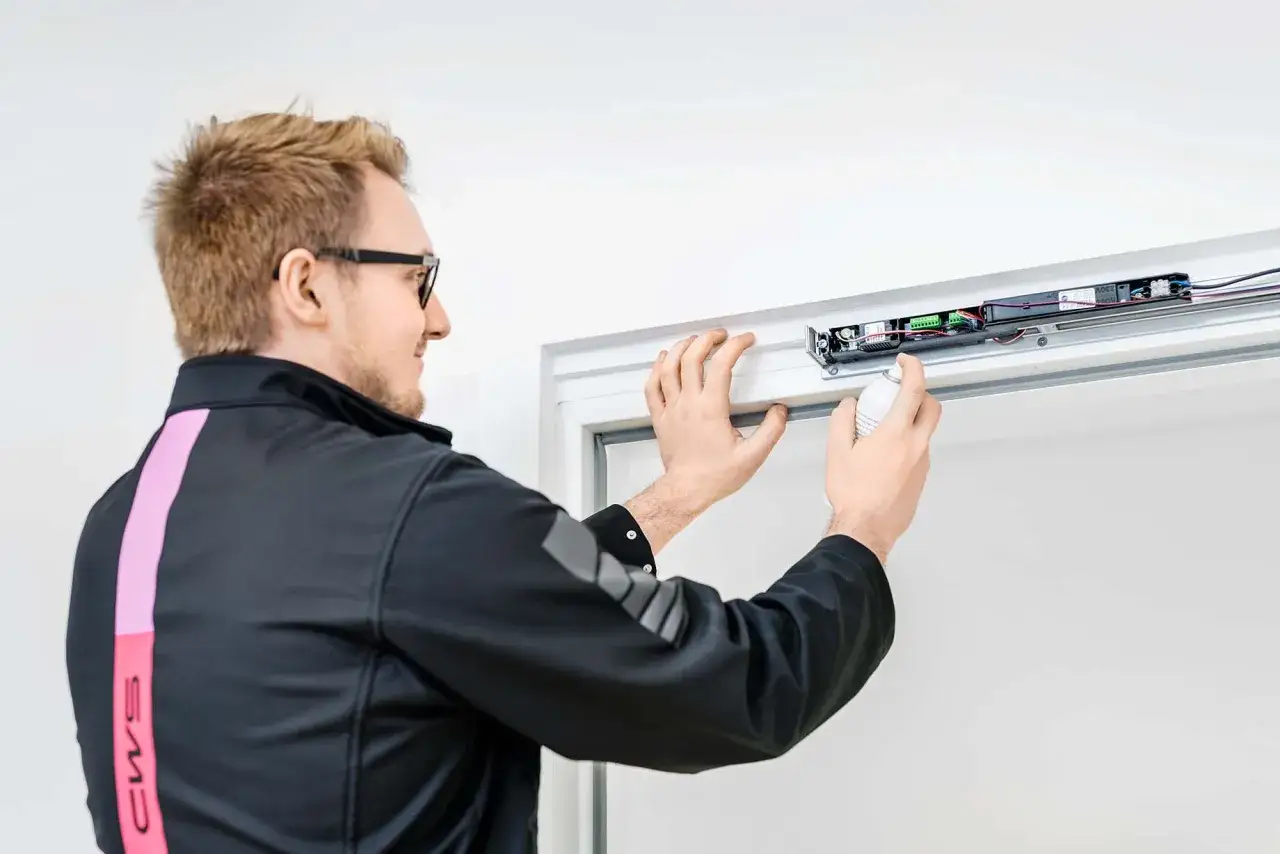 Techniker sprüht auf die Elektronik einer automatischen Tür. Regelmäßige Wartung von Feststellanlagen sorgt für reibungslosen Betrieb.