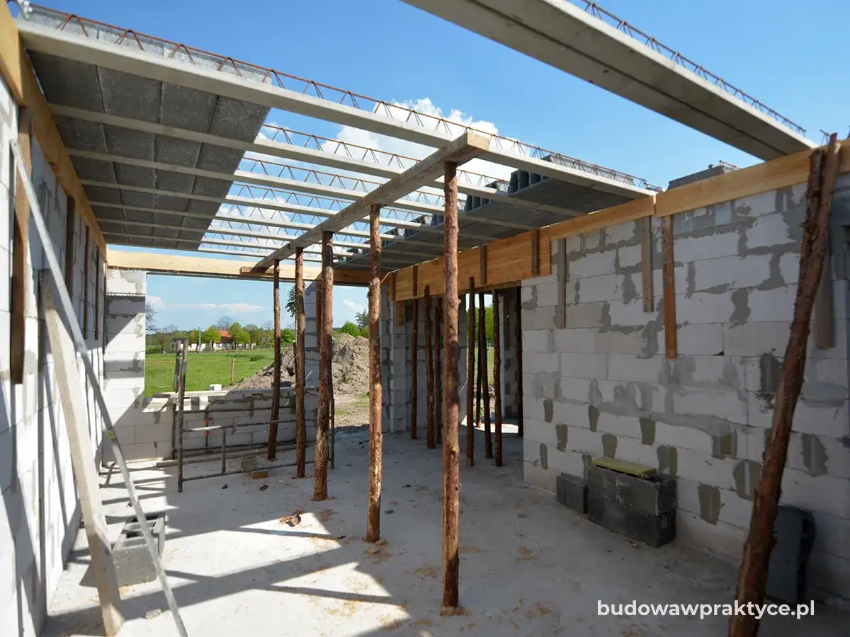 Budowa domu w toku. Widać strop gęstożebrowy, ściany z bloczków betonowych i drewniane podpory.