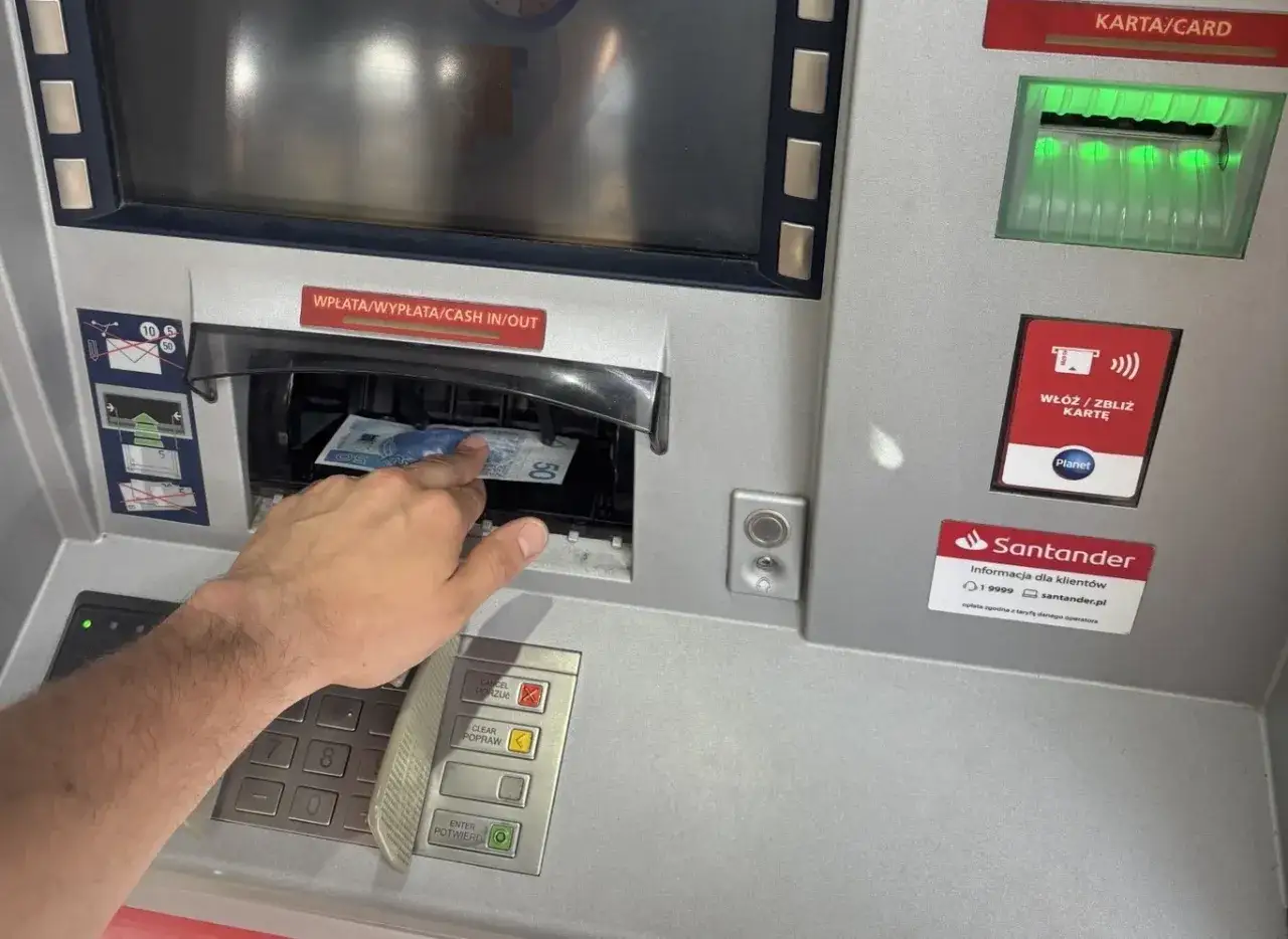Ręka wyciąga banknot 50 zł z bankomatu. Zastanawiasz się, ile można wyplacic w Żabce? To nie bankomat Żabki, ale bankomat Santander.