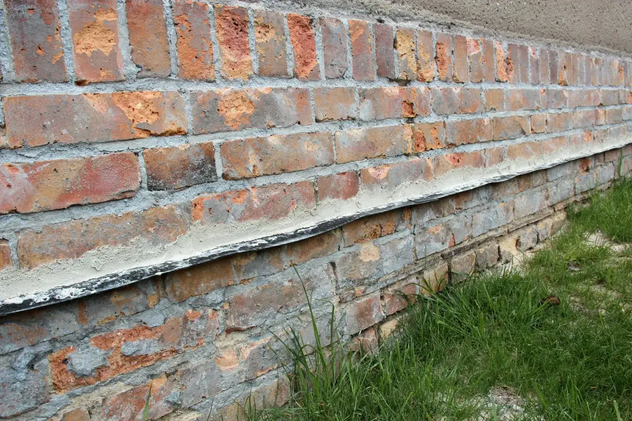 Alte Ziegelwand mit einer horizontalen Sperre, die Feuchtigkeit abh&auml;lt. Gras w&auml;chst am Fu&szlig; der Wand.