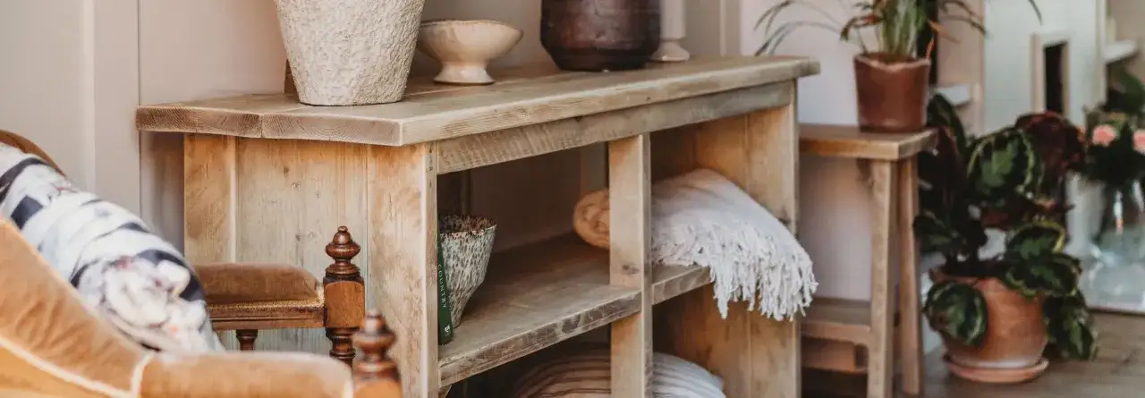 A wooden console table with shelves, showcasing rustic styles. Decorated with pots, throws, and a book.