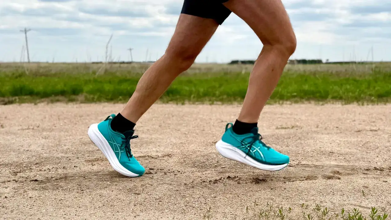 Gambe di un corridore in movimento su un sentiero sterrato. Le scarpe da running turchesi e bianche sono in primo piano, mostrando cos'è il running: libertà e movimento all'aria aperta.