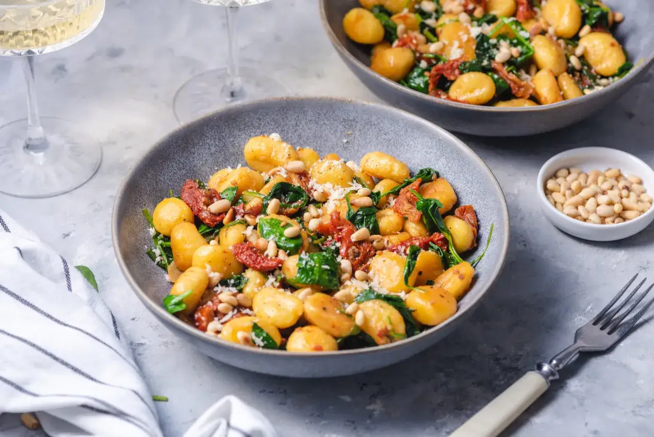 Pyszne gnocchi ze szpinakiem, suszonymi pomidorami i orzeszkami pinii, posypane parmezanem. Idealne danie na szybki obiad.