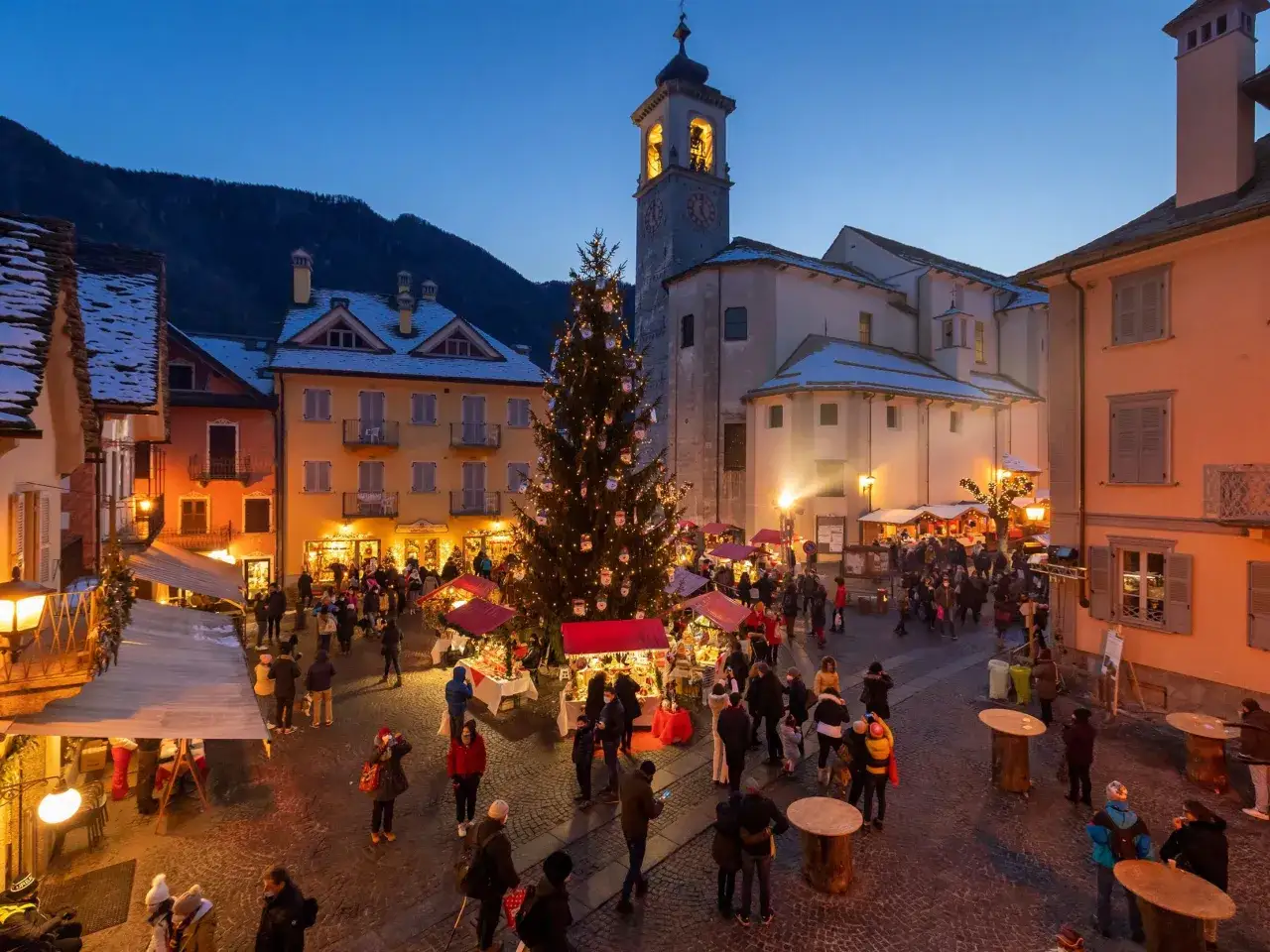 Mercatino di Natale in una piazza alpina, un'ottima idea per le città da visitare a dicembre. Albero addobbato, bancarelle e gente passeggia.