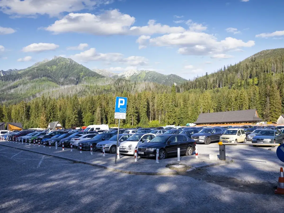 Parking pełen samochodów, gotowych na wycieczkę nad Morskie Oko. Góry i lasy w tle zapraszają do wędrówki.