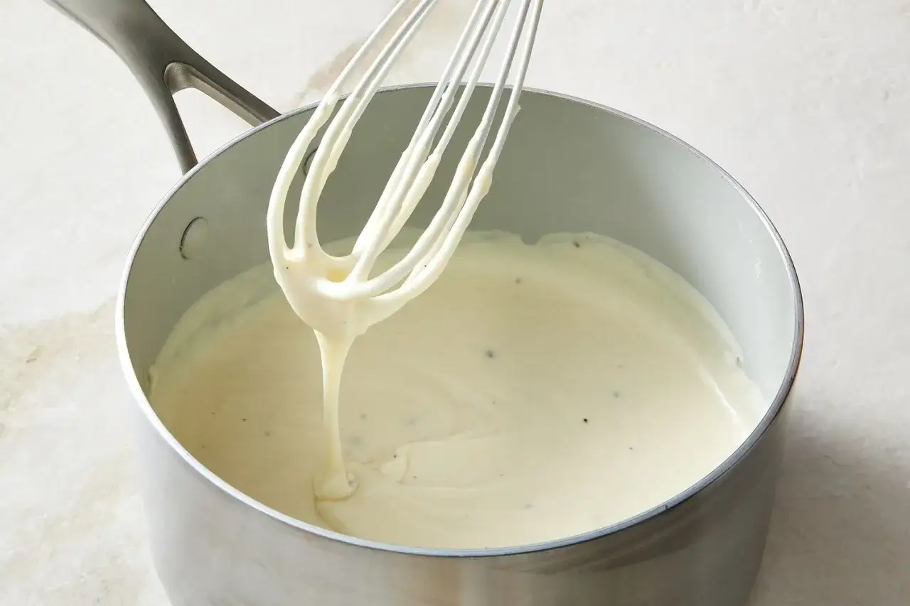 Cremige Bechamelsauce für Lasagne wird in einem Topf mit einem Schneebesen zubereitet.